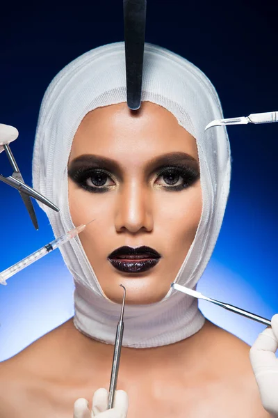 Beauty Aesthetic Plastic Surgery Patient with bandage, surgical tools, equipment around head. Studio Lighting gradient Blue Background, Concept Propaganda Clinic High Fashion Set