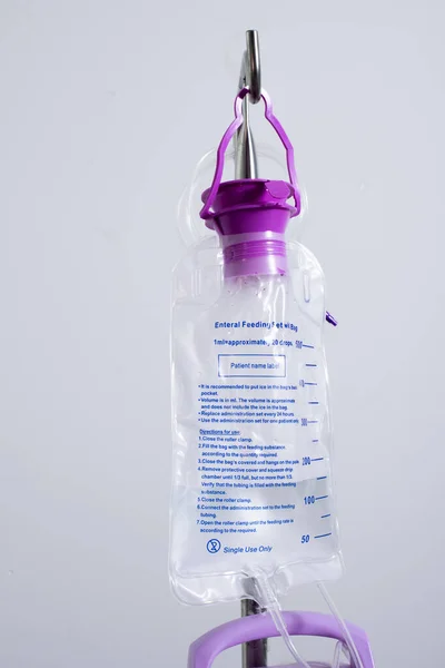 Feeding Pump medical device purple color to supplement nutrition liquid food to tube Enteral feeding fluid set bag with clamp hanging on stand.