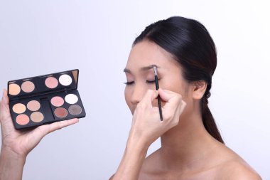 Makyaj pudrası ve göz fırçası sürüyorum. Kozmetik renk paletli bronz tenli genç bir kız için göz farı. Kapat, stüdyonun gri arka planını aydınlat