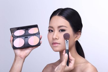 Makyaj pudrası ve göz fırçası sürüyorum. Kozmetik renk paletli bronz tenli genç bir kız için göz farı. Kapat, stüdyonun gri arka planını aydınlat