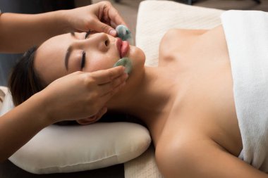 Mix Race Kafkas Asyalı kadının yüz masajı, Terapist Spa vücut kadını müşteriye çakra dengeleyici masaj masajı yapıyor sıcak Jade taşı etkisi iç duygu stresi