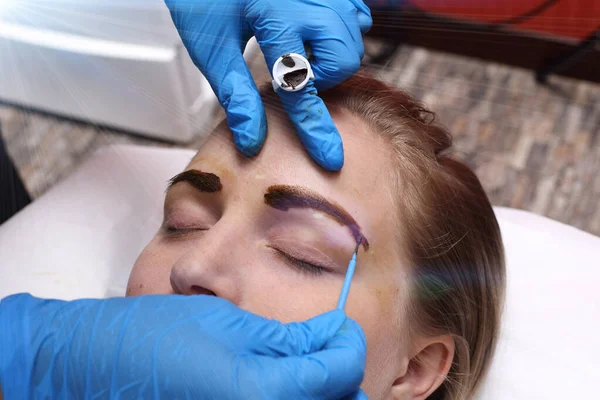 Professional Beautician Asian woman applying Tottoo, Brow Microblading to caucasian customer eyebrows to make permanent color makeup or tattooing line look real in beauty salon, copy space text logo