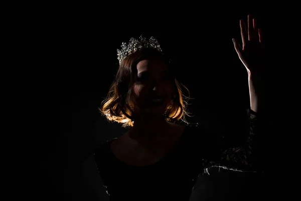 Portrait Silhouette Shadow Back Rim Light of Miss Pageant Beauty Queen Contest Silver Diamond Crown wave hand express feeling smile, studio lighting dark black background, turn front face to camera