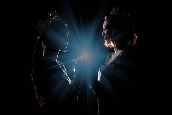 Two Silhouette Shadow Back Rim Light of Miss Pageant Beauty Queen Contest with Silver Diamond Crown hold pray together for final moment announce Winner prize, studio lighting dark black background