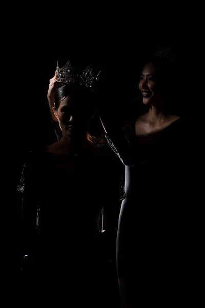 Two Silhouette Shadow Back Rim Light of Miss Pageant Beauty Queen Contest put Silver Diamond Crown on Winner final moment most beautiful woman in world universe, studio lighting dark black background