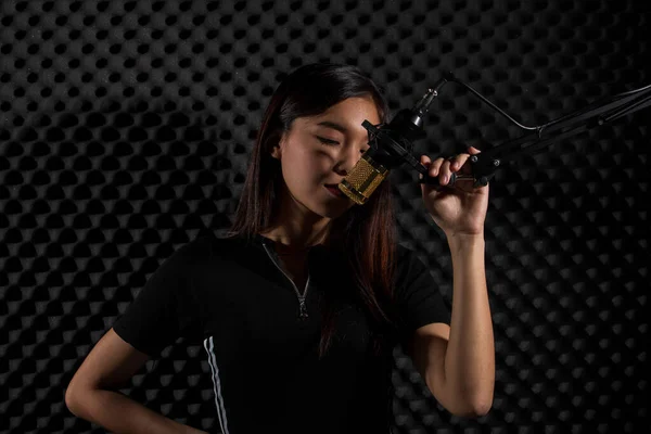 Asian Adult Woman sing a song loudly with power sound over hanging microphone condenser filter in black shirt. Egg Crate Studio lighting shadow silhouette Sound Proof Absorbing wall room