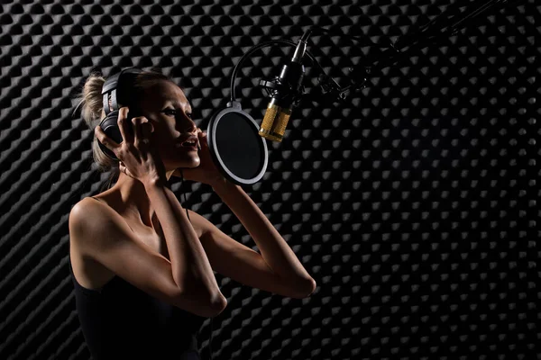 Mix Race skinny Woman blonde short hair earmuff headphone sing a song loudly with power sound over hanging microphone condenser. Egg Crate Studio low lighting shadow Sound Proof Absorbing wall room