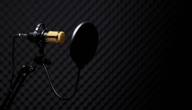 Mikrofon Yoğunlaştırıcı, filtresi olan altın mikrofon karanlık ses stüdyosundaki ses emici duvar odasının üzerinde asılı. Düşük çözünürlüklü gölge siluet stüdyosunun arka plan ışıklandırma alanı.