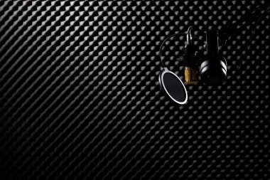 Mikrofon Yoğunlaştırıcı, filtre kulaklı altın mikrofon. Kulaklık, karanlık ses stüdyosundaki ses emici duvar odasının üzerinde asılı. Düşük çözünürlüklü gölge siluet stüdyosunun arka plan fotokopi alanı.