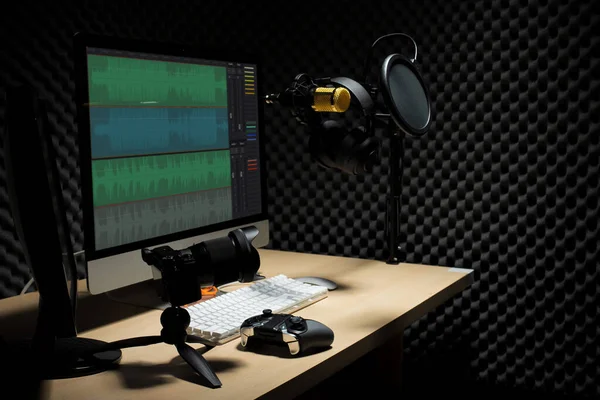 マイクコンデンサ 波モニターキーボードマウスゲームパッドコントローラと暗いオーディオスタジオでヘッドフォン 低露出照明背景コピースペースとサウンド吸収壁の部屋に金のマイクハング — ストック写真