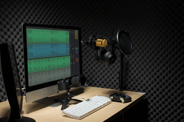 マイクコンデンサ 波モニターキーボードマウスゲームパッドコントローラと暗いオーディオスタジオでヘッドフォン 低露出照明背景コピースペースとサウンド吸収壁の部屋に金のマイクハング — ストック写真