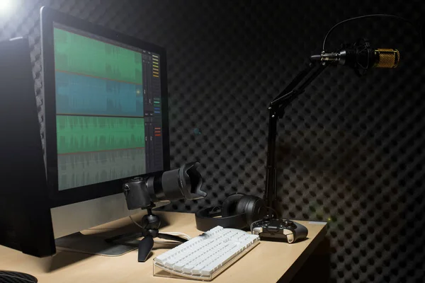 マイクコンデンサ 波モニターキーボードマウスゲームパッドコントローラと暗いオーディオスタジオでヘッドフォン 低露出照明背景コピースペースとサウンド吸収壁の部屋に金のマイクハング — ストック写真