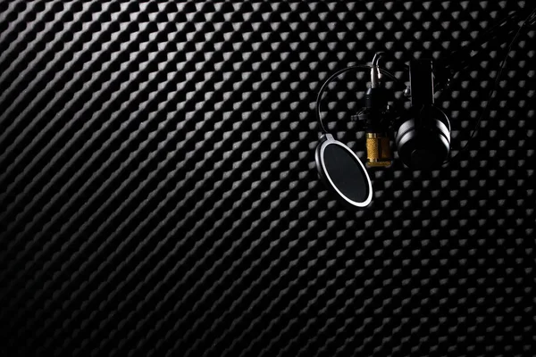 マイクコンデンサー フィルター付きの金のマイクヘッドフォンイヤーマグカップは暗いオーディオスタジオの吸音壁の部屋に掛け 低露出の影のシルエットスタジオ照明背景コピースペース — ストック写真