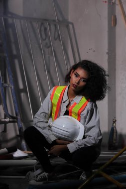 Güzel Asyalı mimar kadın beyaz başlıklı kıvırcık saçlı, inşaat odasındaki büyük güvenlik enkazı temizliyor ve yenileme yapıyor, konsept kadın moda sonrası sahne yapabilir.