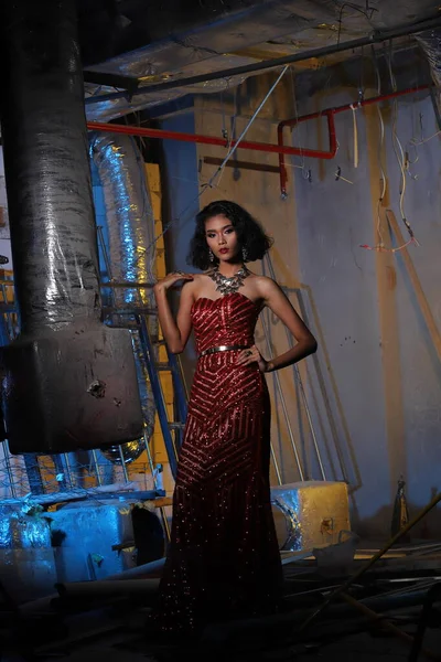 Evening Gown Ball Dress in Asian beautiful woman with fashion make up face eyes love heart black hair, red sequin evening gown in debris engineer construction site copy space