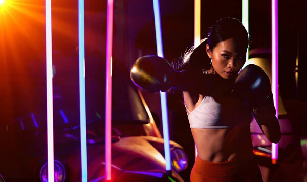 Спортсмен-азиатка тренируется бить боксёра в серебряных перчатках. Упражнения Office Girl в современном цвете Неон "Муай тай Тук Тук автомобиль" Бокс тренажерный зал фон, низкая экспозиция высокой насыщенности
