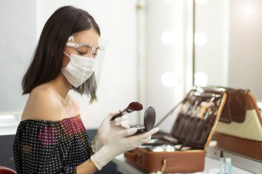 Kariyerin Yeni Normal 'ı insanlarla çalışıyor, makyaj sanatçısı kendini ve müşterisini korumak için lastik eldiven, maske ve Face Shield takmak zorunda. Genç Asyalı Kadın fırça tozu tutuyor
