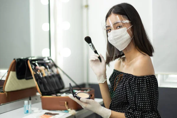 Covid New Normal of Career working with people, make up artist has to wear rubber glove, surgical mask and Face Shield to protect both herself and customer. Young Asian Woman look at camera