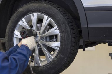 Pnömatik aletli profesyonel bir oto tamircisi araba servisinin tekerleklerini değiştirmek için cıvataları gevşetiyor..