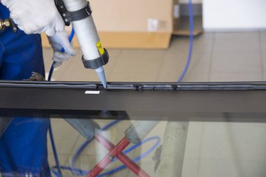 Profesyonel bir tamirci araba atölyesindeki arabanın ön camını değiştiriyor. El tamircisi bir alet tutuyor. Otomobil gözlüklerinin değiştirilmesi.