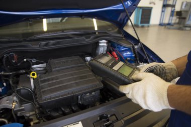 A professional car mechanic works in a car service. Mechanic service using Multimeter to check the voltage level in a car battery Car diagnostics. clipart