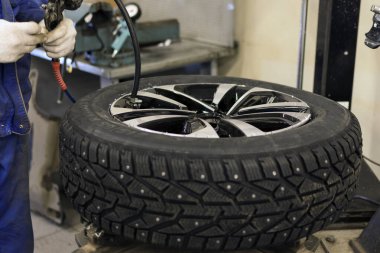 Mevsimlik kış lastiği servisi. Araba servisinde profesyonel tamirci. Lastik değiştirmek için makineye takılan bir araba tekerleği. İş yerinde bir tamirci.