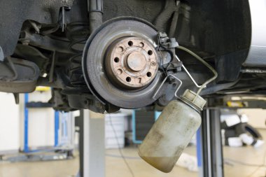Araba servisinde araba tamiri. Aracın fren sıvısını değiştirmek. Fren diski ve bir tamirhanenin arka planına karşı özel bir araç.
