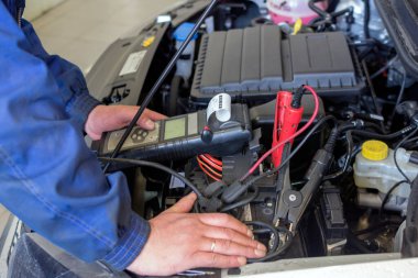 Profesyonel bir araba tamircisi araba servisinde çalışır. Araba aküsünün voltaj seviyesini kontrol etmek için Multimetre kullanan mekanik servisi.