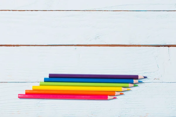 six-color rainbow from pencils on blue wooden background