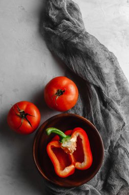 Sebzeli ahşap tabak, domates, biber, açık beton arka planda kumaşlı soğan.