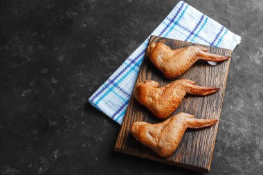 Ahşap bir masanın üzerinde tütsülenmiş tavuk kanadı ve arka planı koyu renk.