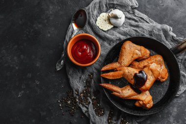 Ketçaplı füme tavuk kanadı, sarımsak ve acı biber. Siyah beton arka plan. Mangal. Yukarıdan manzara. Metin için boşluk.