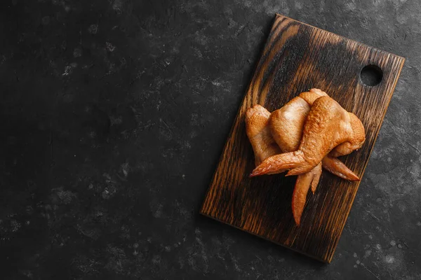 Smoked chicken wings on a wooden table with a towel and a dark background top view