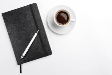 Kapalı ve açık bir not defteri, bir fincan kahve ve beyaz arka planda çiçek manzaralı bir kalemle. Metin için boşluk
