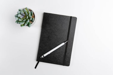 Kapalı ve açık bir not defteri, bir fincan kahve ve beyaz arka planda çiçek manzaralı bir kalemle. Metin için boşluk