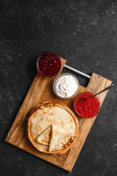 Maslenitsa Maslenitsa week is a holiday of food. Stack of Russian pancakes Pancakes with red caviar, fresh sour cream and raspberry jam. Rustic style, top view