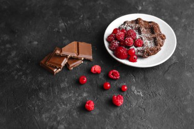 Kakaolu ev yapımı çikolatalı waffle ve ahududulu bir tabakta pudra şekeri ve metin için arka planda koyu bir alanda çikolata.