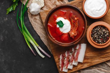 Ukrayna Borsch 'u. Pancar çorbası. Ukrayna mutfağı. Ahşap bir tabakta tuzlanmış pastırma, ekmek ve otlarla birlikte. Karanlık arka planda. Yukarıdan manzara. Metnin için boş yer. Bir kase kremalı kırmızı pancar çorbası..