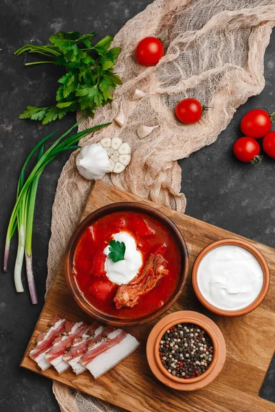 Ukrayna Borsch 'u. Pancar çorbası. Ukrayna mutfağı. Ahşap bir tabakta tuzlanmış pastırma, ekmek ve otlarla birlikte. Karanlık arka planda. Yukarıdan manzara. Metnin için boş yer. Bir kase kremalı kırmızı pancar çorbası..