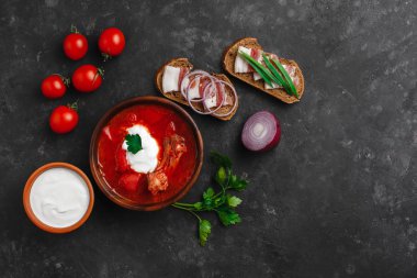 Ukrayna Borsch 'u. Pancar çorbası. Ukrayna mutfağı. Ahşap bir tabakta tuzlanmış pastırma, ekmek ve otlarla birlikte. Karanlık arka planda. Yukarıdan manzara. Metnin için boş yer. Bir kase kremalı kırmızı pancar çorbası..