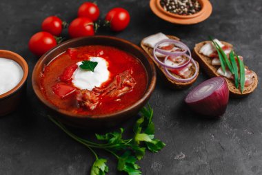 Ukrayna Borsch 'u. Pancar çorbası. Ukrayna mutfağı. Ahşap bir tabakta tuzlanmış pastırma, ekmek ve otlarla birlikte. Karanlık arka planda. Yukarıdan manzara. Metnin için boş yer. Bir kase kremalı kırmızı pancar çorbası..