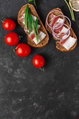 Tuzlu domuz yağlı sandviç, yeşil soğanlı siyah ekmek, sarımsak ve domates. Karanlık arka planda. Yukarıdan manzara. Metin için boşluk.