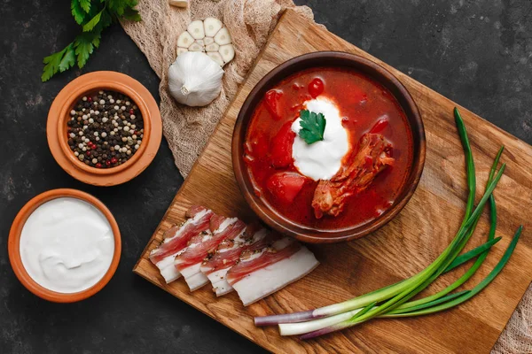Ukrayna Borsch 'u. Pancar çorbası. Ukrayna mutfağı. Ahşap bir tabakta tuzlanmış pastırma, ekmek ve otlarla birlikte. Karanlık arka planda. Yukarıdan manzara. Metnin için boş yer. Bir kase kremalı kırmızı pancar çorbası..
