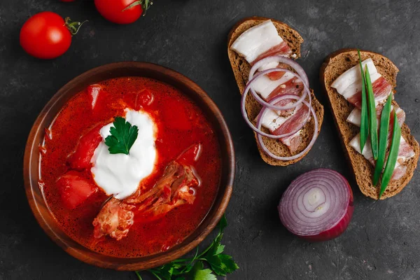 Ukrayna Borsch 'u. Pancar çorbası. Ukrayna mutfağı. Ahşap bir tabakta tuzlanmış pastırma, ekmek ve otlarla birlikte. Karanlık arka planda. Yukarıdan manzara. Metnin için boş yer. Bir kase kremalı kırmızı pancar çorbası..
