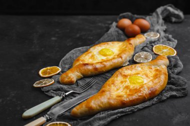 Yumurta ve peynirli Khachapuri. Gürcistan mutfağı. Üzerinde un ve paçavra olan eski bir siyah arka planda. Metin için boş alan. Yukarıdan manzara. Yan görünüm.