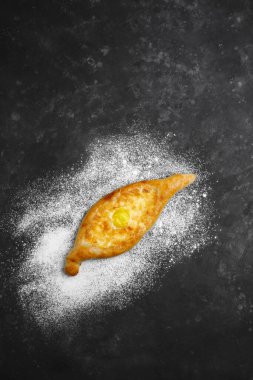 Yumurta ve peynirli Khachapuri. Gürcistan mutfağı. Üzerinde un ve paçavra olan eski bir siyah arka planda. Metin için boş alan. Yukarıdan manzara. Yan görünüm.