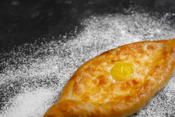 Yumurta ve peynirli Khachapuri. Gürcistan mutfağı. Üzerinde un ve paçavra olan eski bir siyah arka planda. Metin için boş alan. Yukarıdan manzara. Yan görünüm.