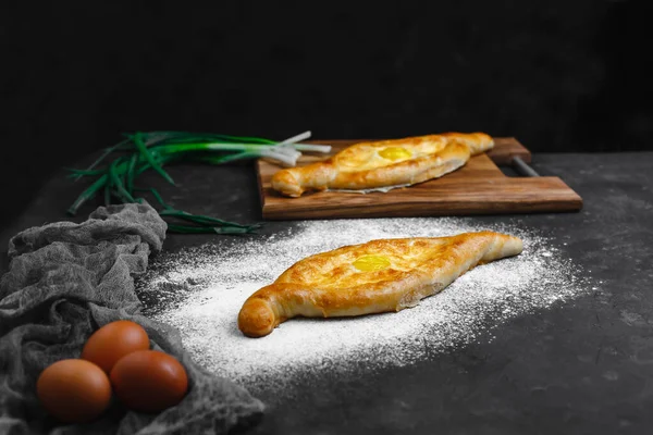 Yumurta ve peynirli Khachapuri. Gürcistan mutfağı. Üzerinde un ve paçavra olan eski bir siyah arka planda. Metin için boş alan. Yukarıdan manzara. Yan görünüm.