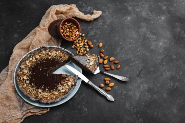 Çikolatalı pasta, çikolatalı pasta, fındıklı tatlı. Kesik bir parça. Kızarmış fıstık, badem ve fındık. Karanlık arka planda. Yukarıdan manzara. Yandan manzara. Metin için boşluk.