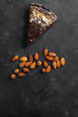 Çikolatalı pasta, çikolatalı pasta, fındıklı tatlı. Kesik bir parça. Kızarmış fıstık, badem ve fındık. Karanlık arka planda. Yukarıdan manzara. Yandan manzara. Metin için boşluk.